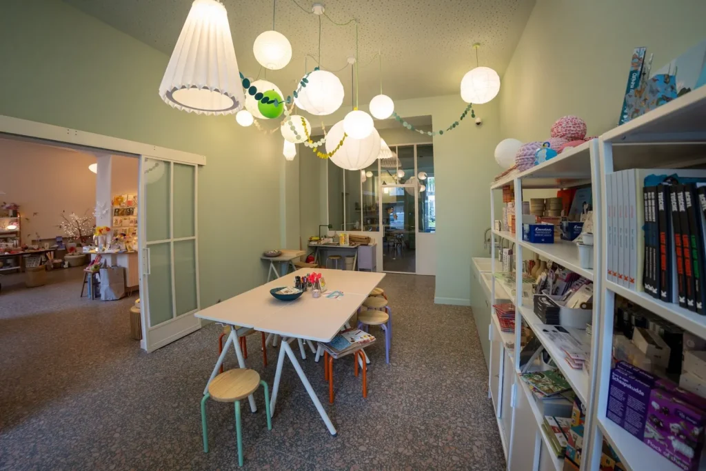 Workshopraum von L' Atelier Papier mit langen Arbeitstischen, Hockern und hängenden Papierlampen