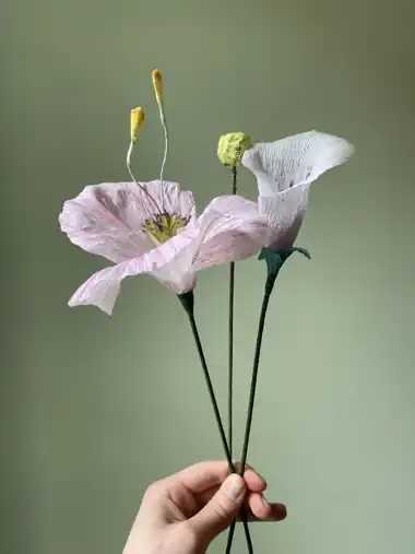 Rosa und weiße Krepppapierblumen mit gelben Knospen vor grünem Hintergrund