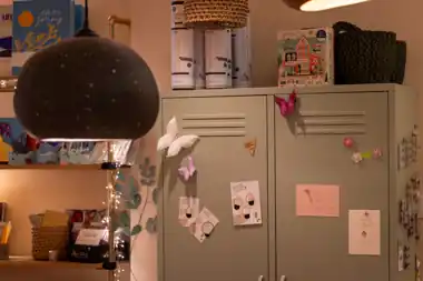 Salbeigrüner Metallspind mit Papierschmetterlingen, Karten und einer Papierlampe im Regal
