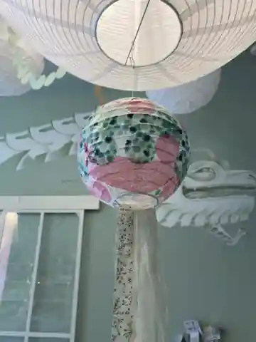 Rosa-grün gemusterter Lampion mit Bändern, der im Laden unter einer weißen Deckenlampe hängt