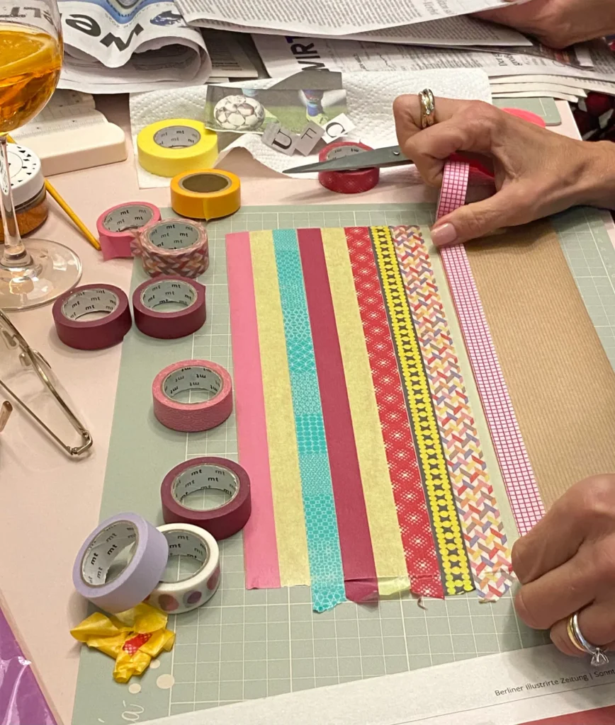 Tape-Art-Collage mit bunten Washi-Tapes und Papierstücken auf dem Arbeitstisch, Hände beim Gestalten