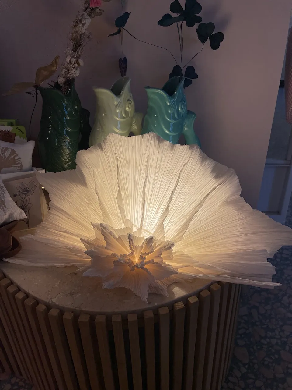 Leuchtende Papierlampe in Fächerform auf einem Holzhocker, feine Falten und ein Stern in der Mitte