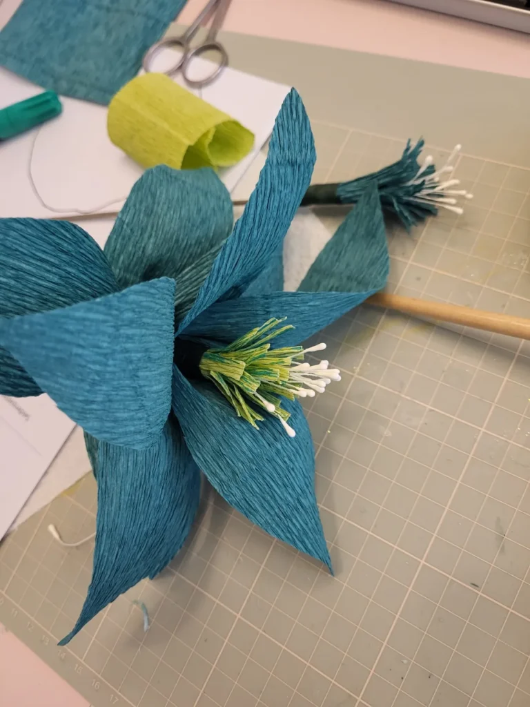 Blaue Blüte aus Krepppapier mit weißen Staubfäden auf einem Arbeitstisch im Workshop