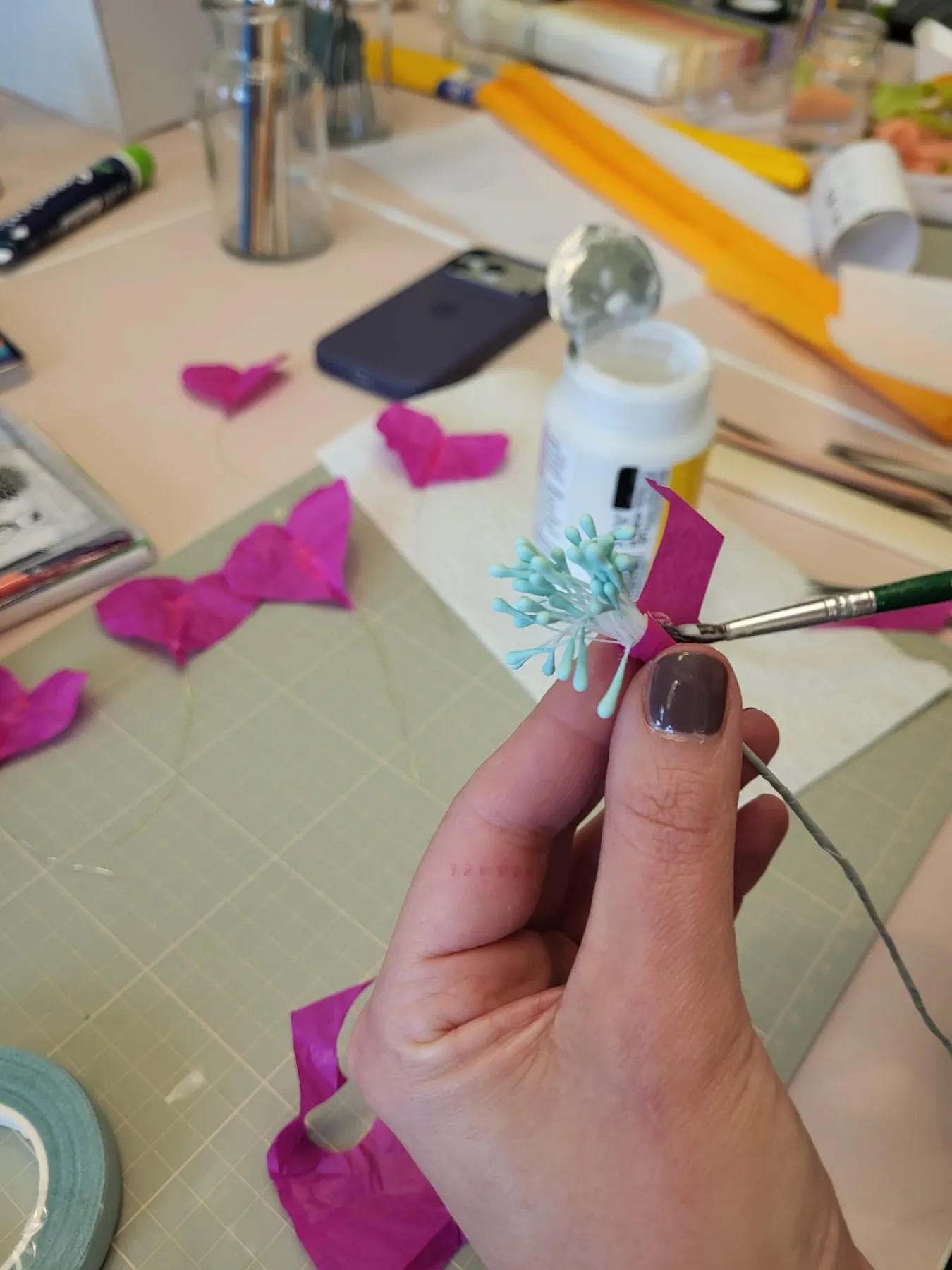 Hände beim Basteln mit magentafarbenem Papier und Klebstoff am Workshop-Tisch