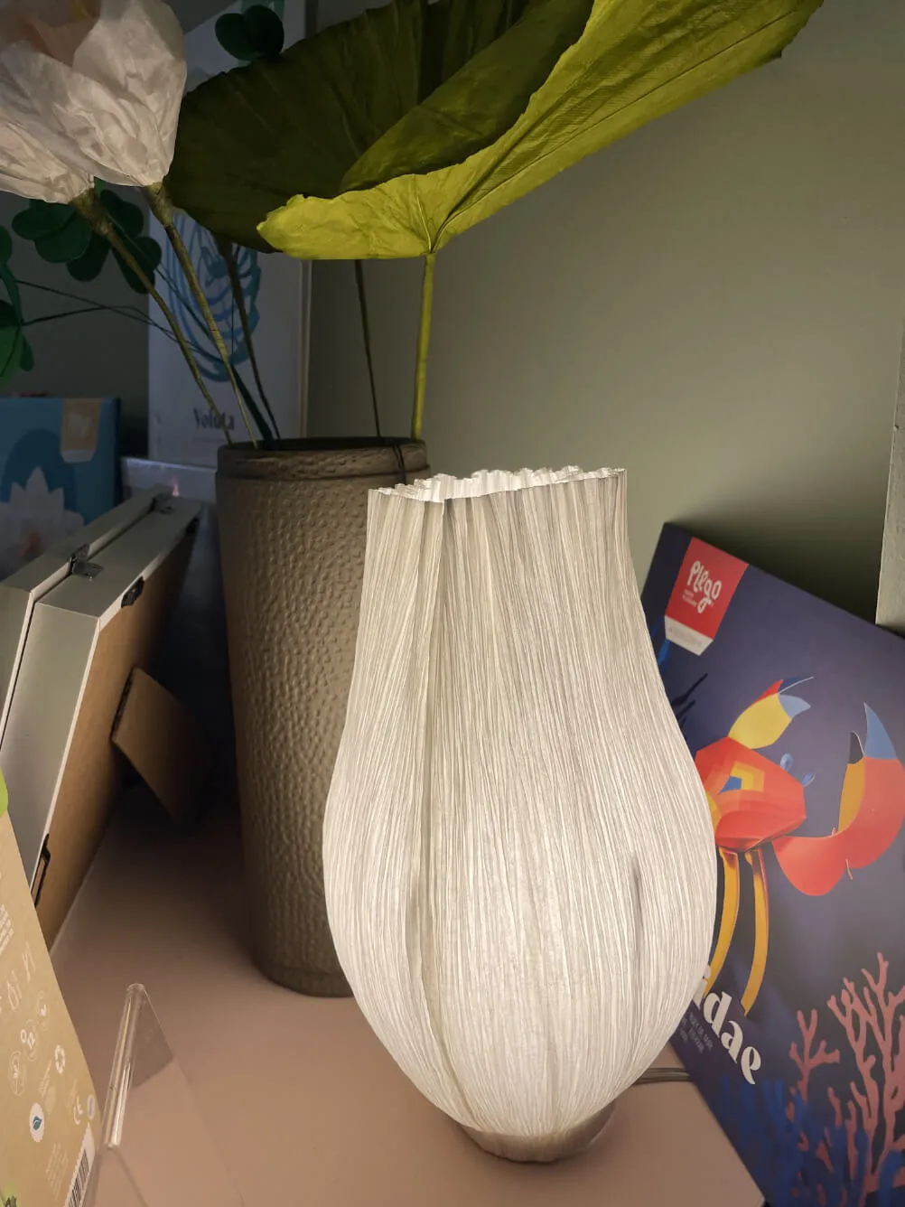 Plissierter Papierschirm vor einem großen grünen Blatt im Regal