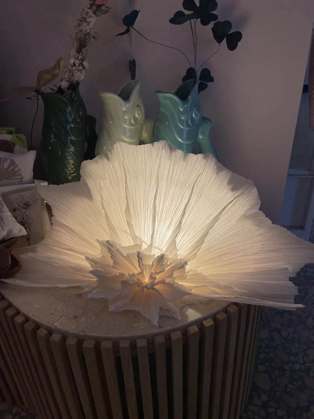Fächerförmige Papierlampe, leuchtend, neben Keramikfischen als Vasen
