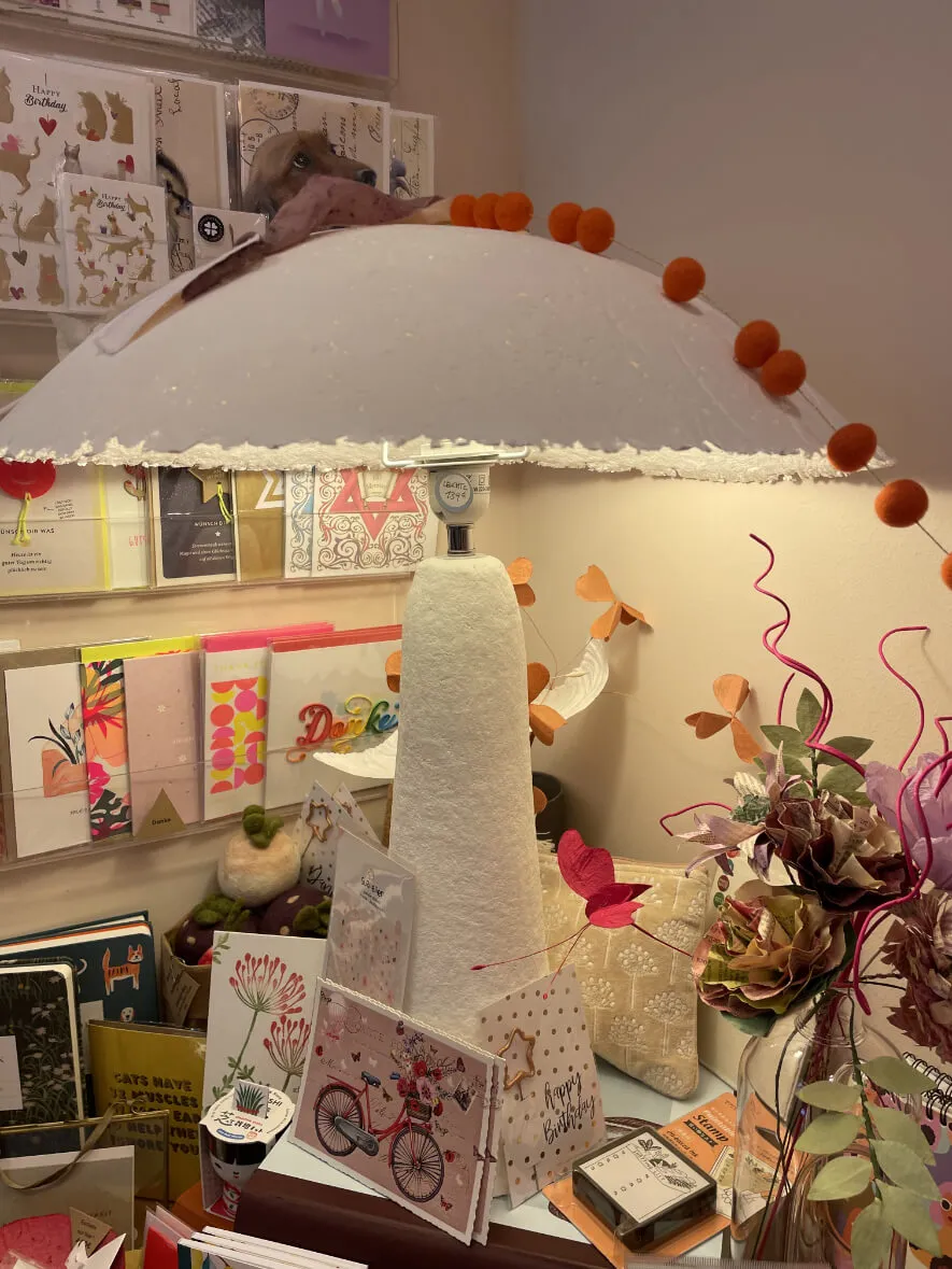 Papierschirm mit Pompons über einem bunten Kartenregal im Laden