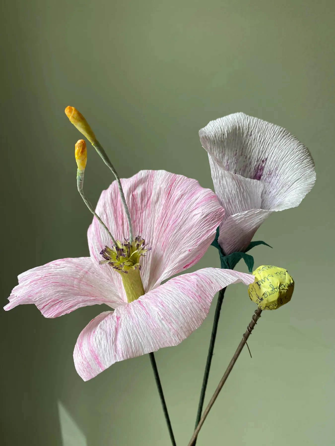 Rosa und cremeweiße Papierblüten mit gelben Staubgefäßen vor grünem Hintergrund, entstanden im Papierblumen-Workshop