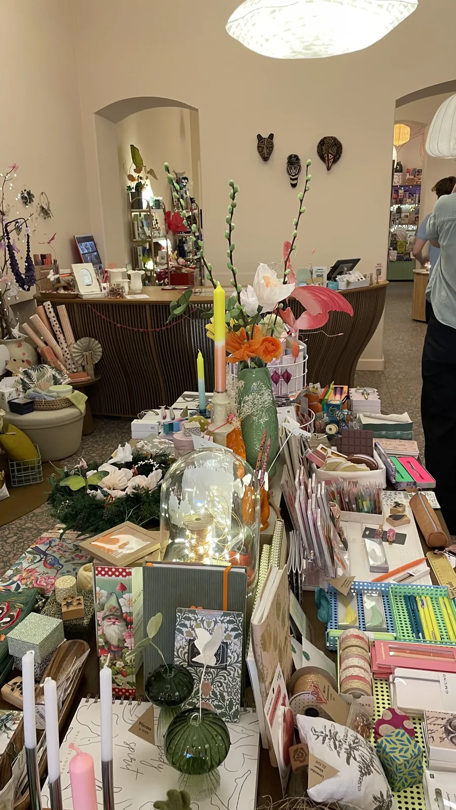 Verkaufsfläche von L' Atelier Papier mit Tisch voller Papeterie, Schreibwaren, Kerzen und Blumen, im Hintergrund Papierlampen