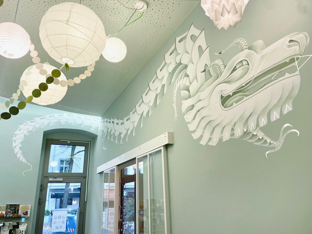 Workshopraum von L' Atelier Papier: Papierdrache an der mintgrünen Wand, darunter weiße Papierlampen und Girlanden